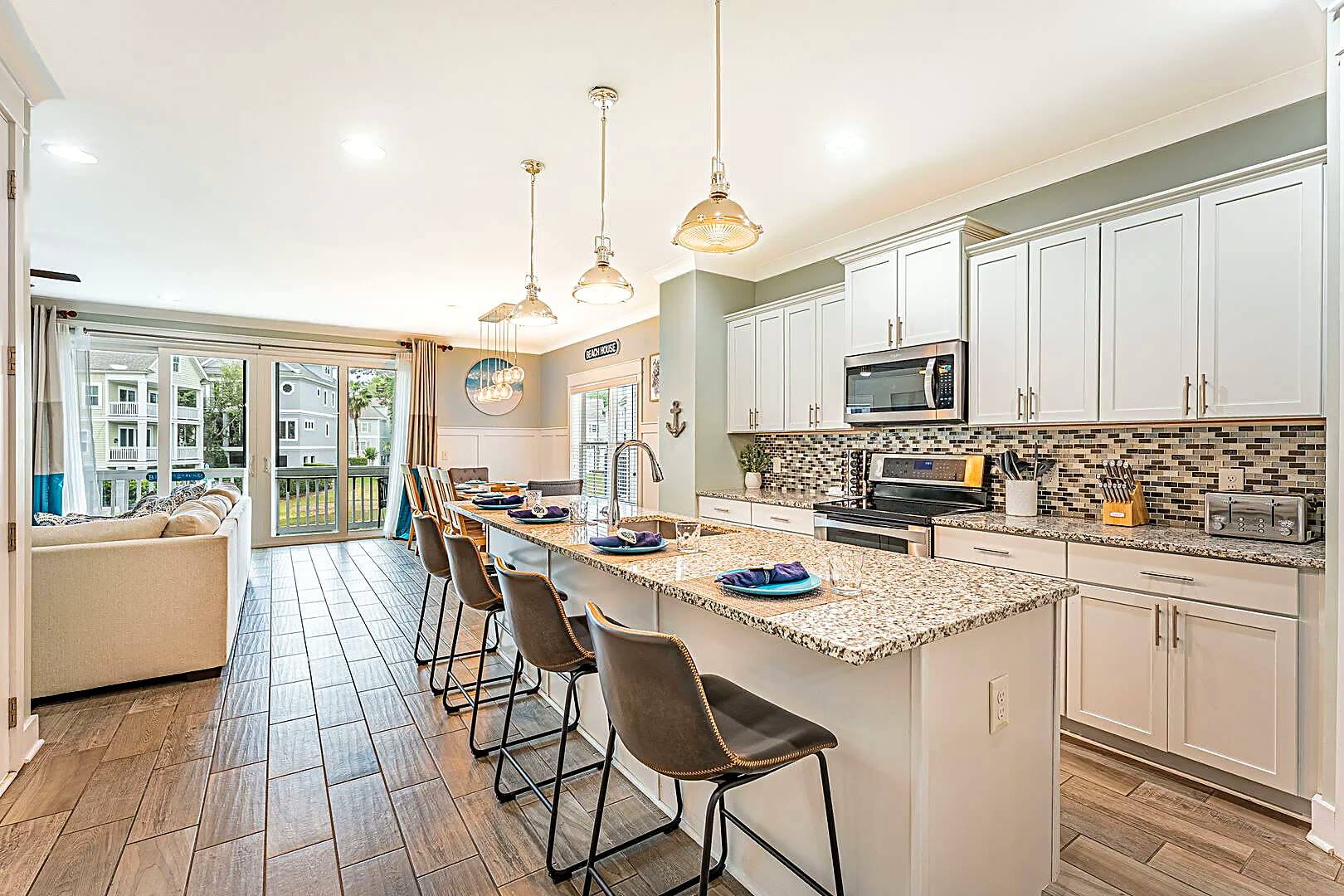 Open kitchen at 122 Sandcastle Court with a granite island seating four, stainless appliances and the living room beyond